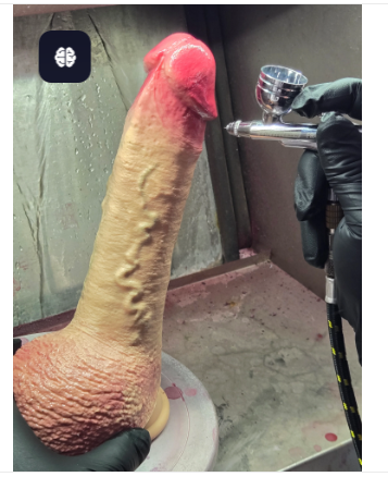 A RealTouch Lab artisan hand-painting a large hyper-realistic silicone product using an airbrush, demonstrating the multi-layer color application process in a professional spray booth.