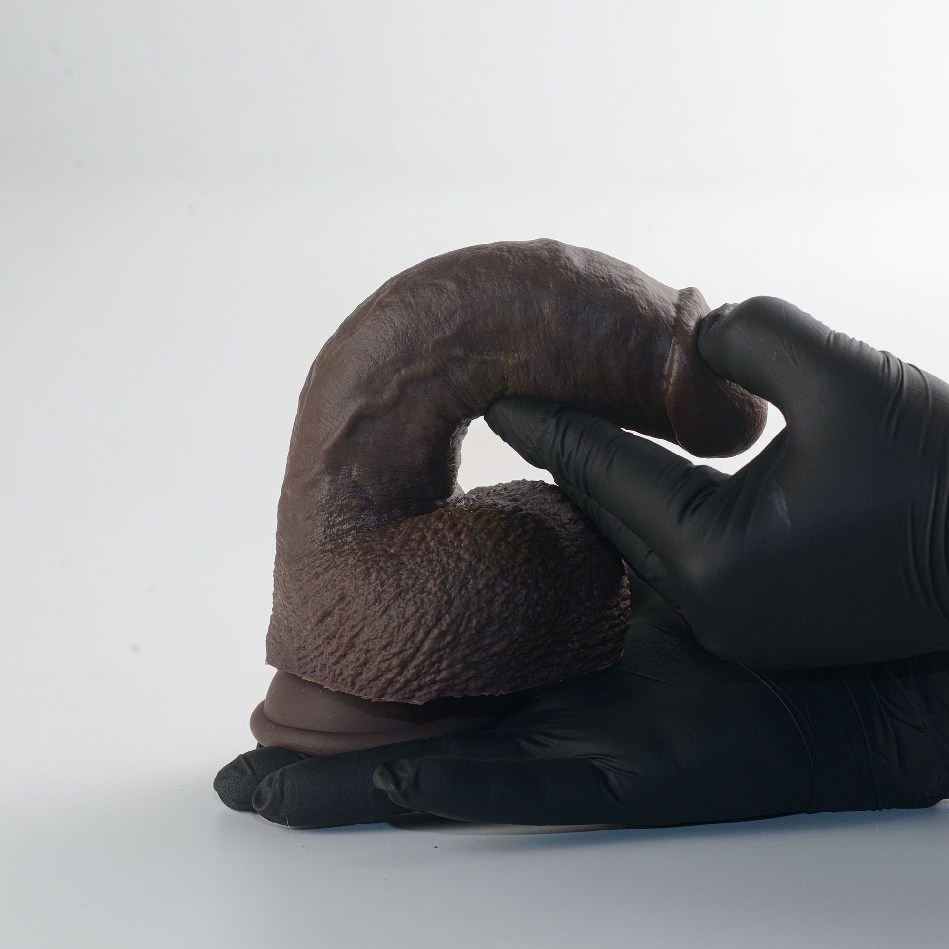 Stage 03 Giganotosaurus dual-density silicone dildo - two gloved hands bending product to demonstrate dual-density flexibility and soft outer layer - body-safe platinum-cured | RealTouch Lab
