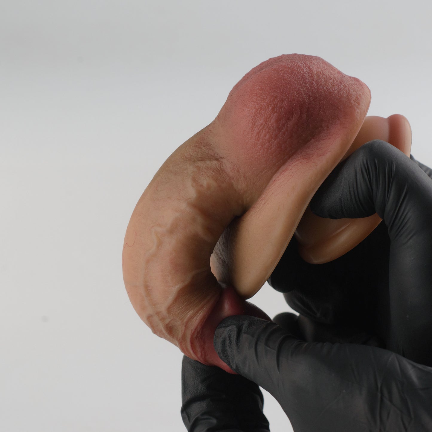 Stage 04 Ossifying Dragon hand-painted silicone dildo - black nitrile gloved hands folding product into U-shape demonstrating extreme dual-density flexibility with no surface cracking - hand-painted finish remains intact under maximum bend - body-safe platinum-cured | RealTouch Lab
