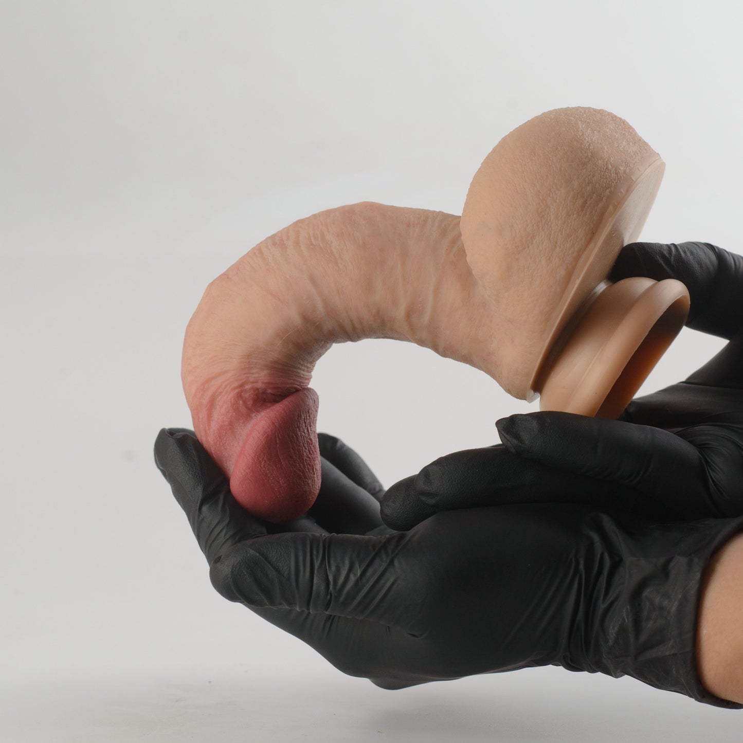 Stage 05 Carnotaurus dual-density silicone dildo with Velvet Shield Coating - two black nitrile gloved hands bending product into full U-shape demonstrating extreme dual-density flexibility, glans nearly touching suction cup base with no cracking or deformation - Velvet Shield Coating remains intact under maximum bend - body-safe platinum-cured | RealTouch Lab
