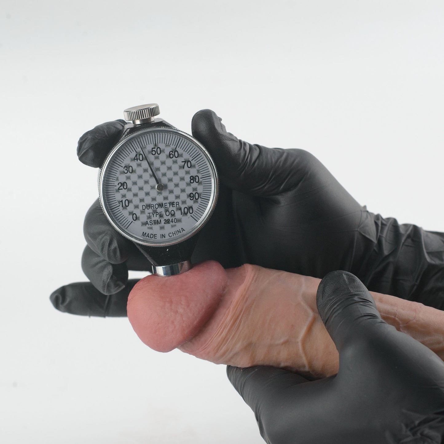 Stage 05 Tyrannosaurus Rex dual-density silicone dildo with Velvet Shield Coating - Shore durometer hardness test at glans showing 43 Shore OO reading on ASTM D2240 gauge held by gloved hands - confirms ultra-soft dual-density body-safe platinum-cured silicone | RealTouch Lab
