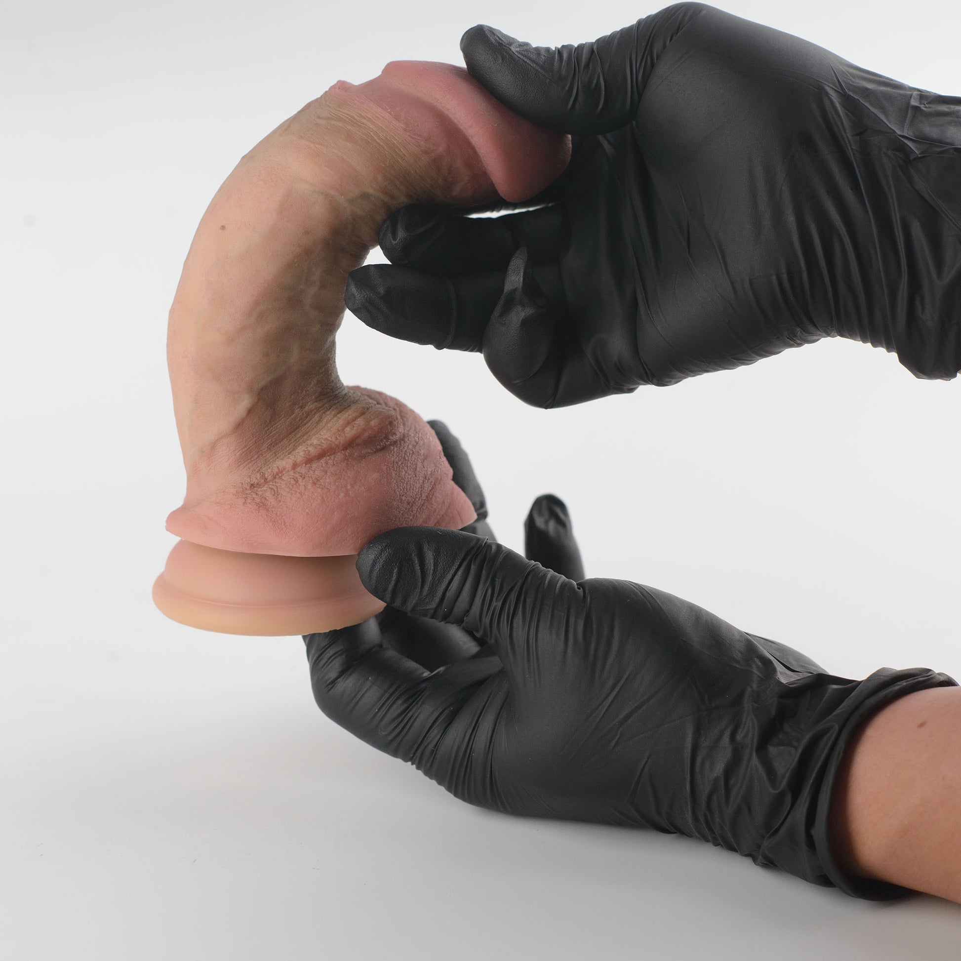Stage 05 Brontosaurus dual-density silicone dildo with Velvet Shield Coating - two black nitrile gloved hands bending product into deep C-shape demonstrating extreme dual-density flexibility, glans nearly touching scrotum with no surface cracking or deformation - Velvet Shield Coating remains intact under maximum bend - body-safe platinum-cured | RealTouch Lab

